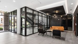 A modern lobby with a glass partition, a staircase, a sofa, and a coffee table. - Pool, Rooftop Deck, City View, Gym + Gated Garage (Nashville)