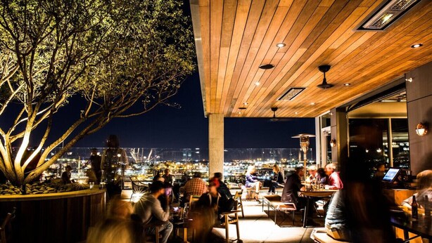 An outdoor dining area with a view of the city at night, wooden ceiling, and tables with chairs. - Pool, Rooftop Deck, City View, Gym + Gated Garage (Nashville)