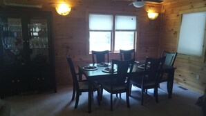 A dining area with a wooden table and chairs, two ceiling fans, and a window with blinds.