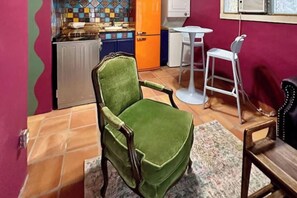 Ein Zimmer mit einem grünen Sessel, einem kleinen Tisch, einem weißen Stuhl und einer gefliesten Wand.