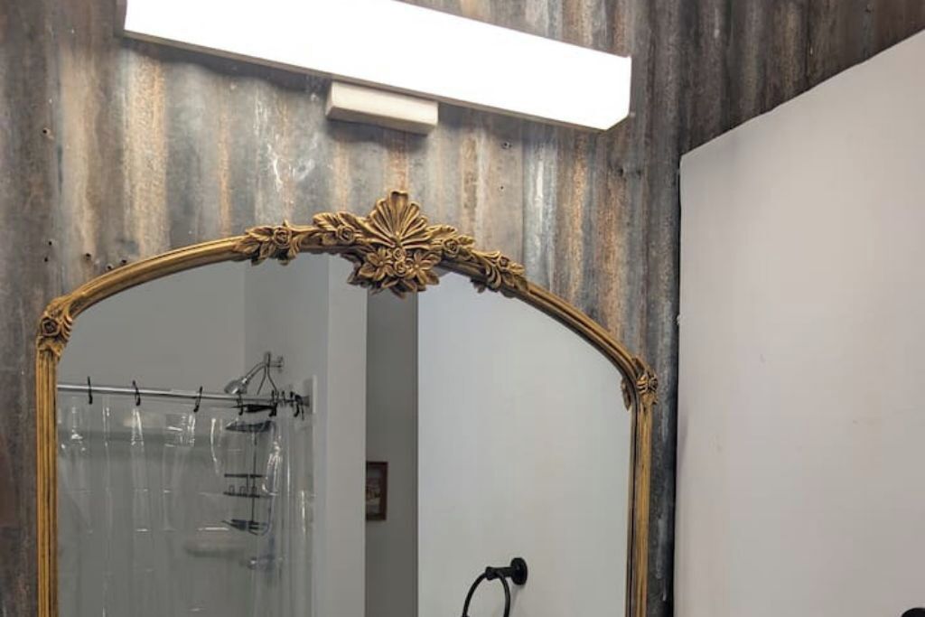A mirror with an ornate gold frame in a room with a wooden wall and a white door.