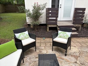 Une terrasse avec deux fauteuils en osier dotés de coussins, une petite table et un banc en bois.