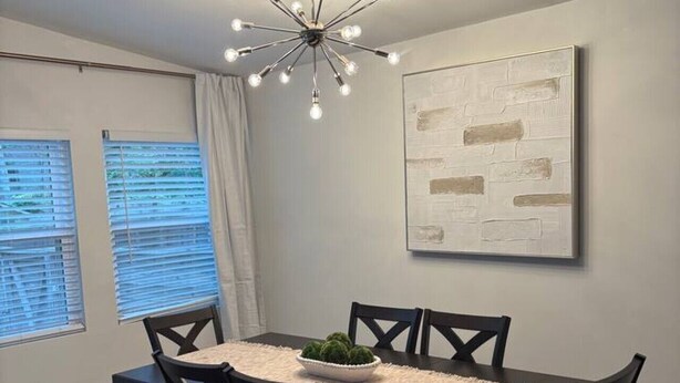 A dining area with a table, chairs, a chandelier, and a painting on the wall. - Modern Beauty in Crestline Park (Birmingham)