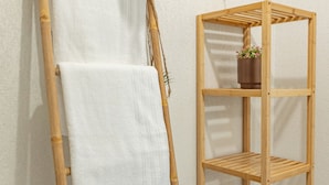 Un baño con un toallero de madera con dos toallas blancas, un estante de madera con una planta en maceta y un inodoro.