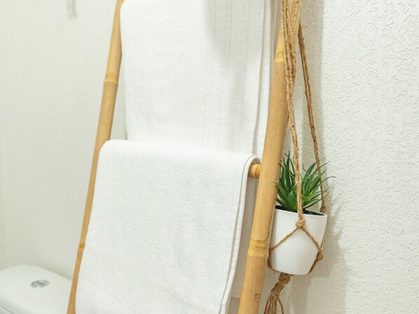 A white towel hanging on a bamboo pole, a small potted plant, and a white toilet in a bathroom.