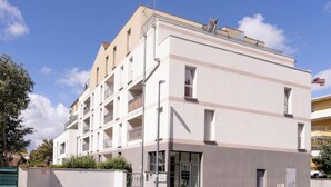 Un edificio residencial de varios pisos, con balcones, una entrada visible y cielo despejado.