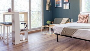 Un dormitorio con cama, escritorio y silla. Hay dos ventanas con cortinas, un estante en la pared y un tapiz de macramé.