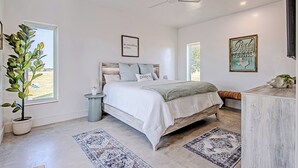 A bedroom with a bed, a ceiling fan, a potted plant, and a framed sign on the wall.