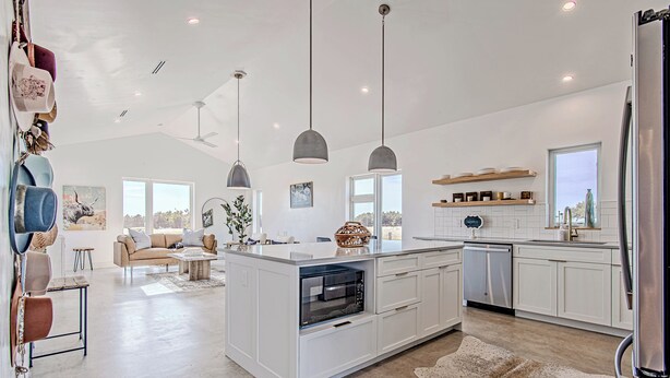 A modern kitchen with white cabinetry, a central island with a built-in oven, pendant lighting, and a large window providing natural light.