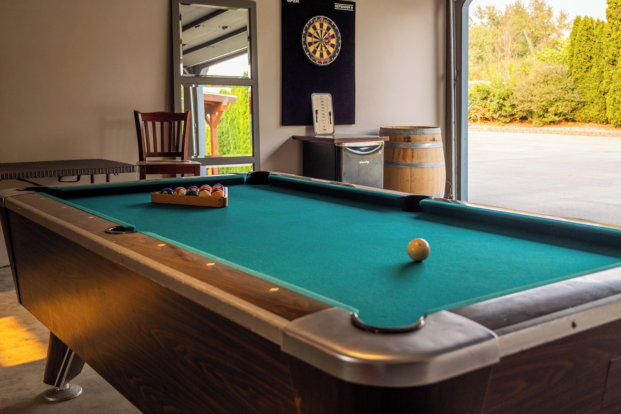 A pool table with a dartboard and a clock on the wall.