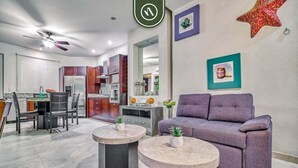 Un salon moderne avec un canapé violet, deux tables rondes et un coin repas avec des chaises.