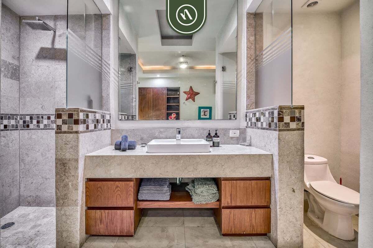 Ein modernes Badezimmer mit einem großen Spiegel, einem Waschbecken und einer Toilette.