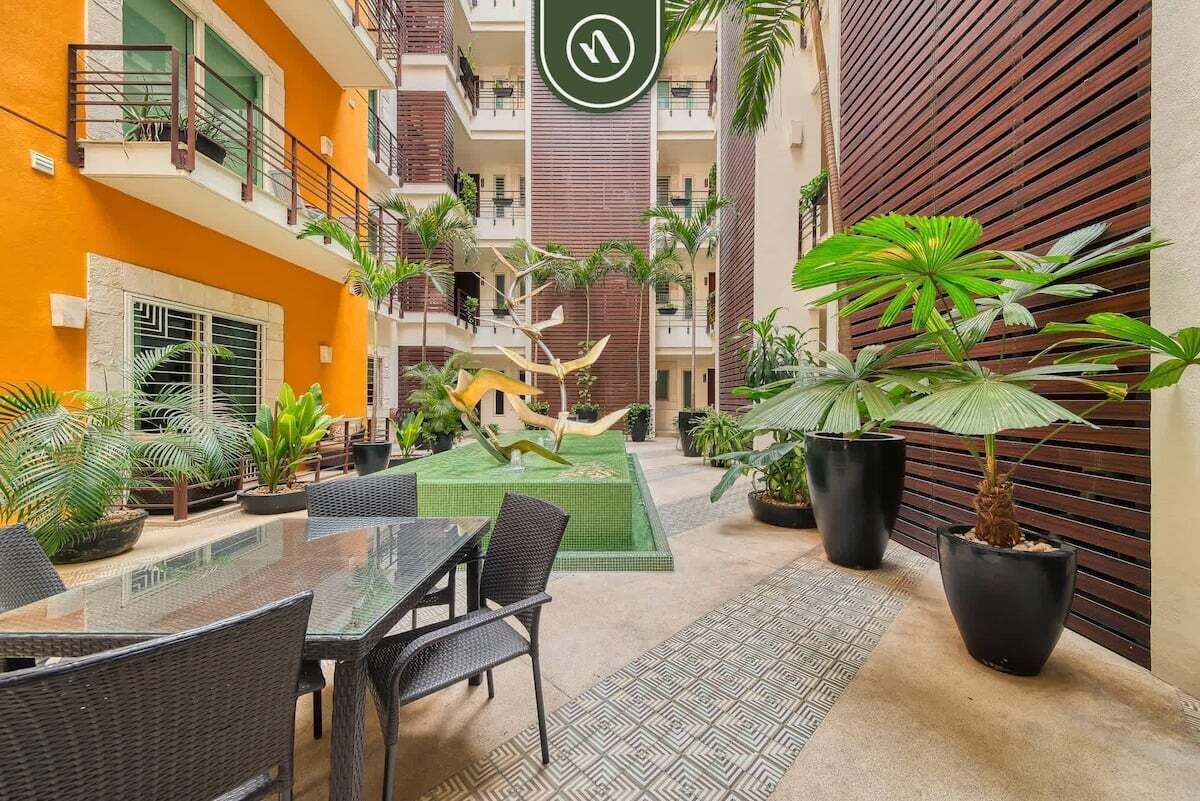 A courtyard with a glass table and chairs, surrounded by potted plants and a decorative sculpture.
