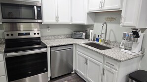 A kitchen with white cabinets, stainless steel appliances, a granite countertop, a sink, and a coffee maker. - Charlie`s by the Bay #3 (New Baltimore)