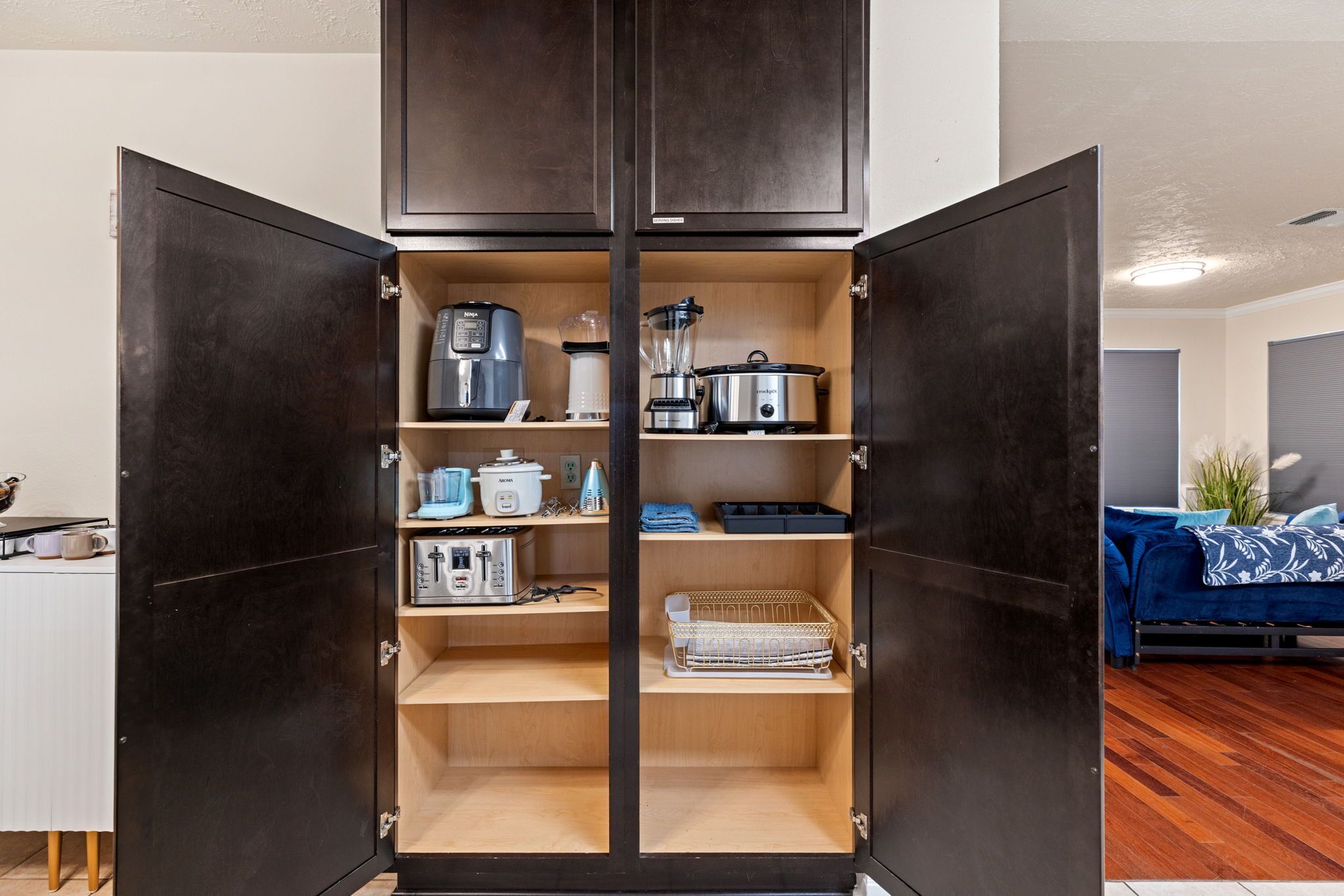 A kitchen with open cabinets, containing a coffee maker, blender, kettle, and other appliances.
