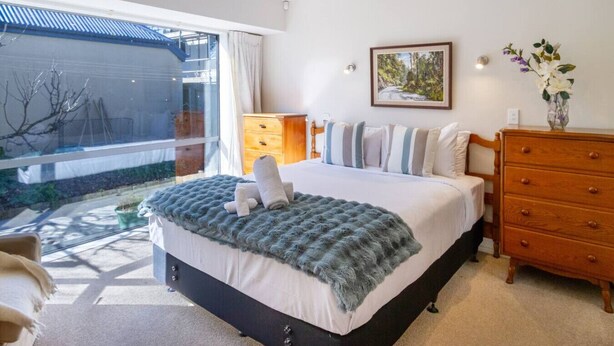 Ein Schlafzimmer mit einem Bett, einer Kommode, einem Fenster mit Gartenblick und einem Bild an der Wand.
