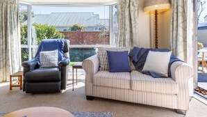Ein Wohnzimmer mit einem schwarzen Ledersessel, einem gestreiften Sofa und einem Tisch. Ein großes Fenster mit Vorhängen, und eine Lampe auf der rechten Seite.