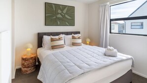Ein Hotelzimmer mit einem großen Bett, zwei Nachttischlampen, einem Kopfteil und einem Fenster mit Vorhängen.