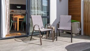 Ein Sitzbereich im Freien mit zwei Stühlen und einem Tisch, eine Glastür, die zu einem Innenraum mit Küche und einem Schild mit der Aufschrift ‚Game Day Lounge‘ führt.