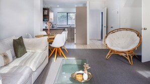 Una sala de estar moderna con un sofá, una mesa de centro de vidrio, una silla de mimbre y un comedor con una mesa y sillas.