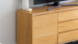 Una habitación moderna con un aparador de madera, un televisor de pantalla plana y un florero con plantas secas.