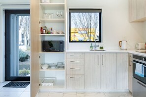 A modern kitchen with white cabinets, a microwave, and a window with a view of a yellow building. - Chic Riccarton Stay with Parking + Outdoor Space (Christchurch)