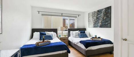 A hotel room with two beds, a large window, and a painting on the wall.