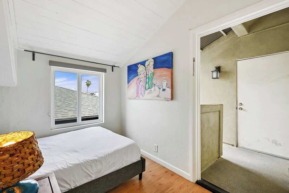A bedroom with a bed, a window, a painting, and a door.