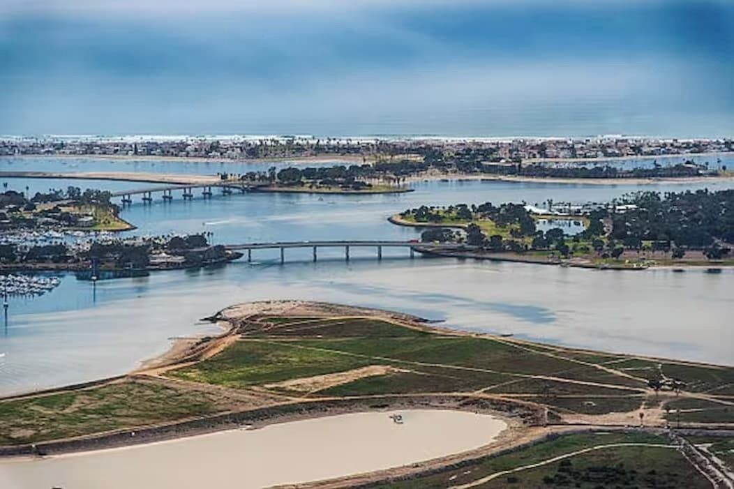 An aerial view of a coastal area with a bridge, water bodies, and a developed shoreline with buildings and greenery.
