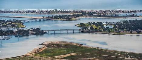An aerial view of a coastal area with a bridge, water bodies, and a developed shoreline with buildings and greenery.