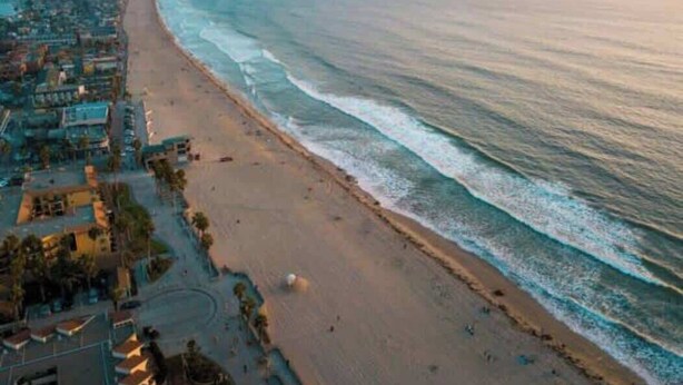 A coastal beach with a long stretch of sand, a few buildings, and a clear view of the ocean. - PB Hot Tub Triplex 5BR, MiniGolf, Games & Parking! (San Diego)