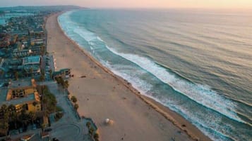 A coastal beach with a long stretch of sand, a few buildings, and a clear view of the ocean.