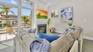 A modern living room with a large window, a fireplace, and a sofa with cushions. - Stunning 4BR Villa with Bay Views & Rooftop Decks! (San Diego)