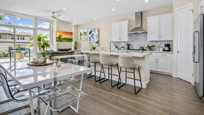 A modern kitchen with white cabinets, a central island with bar stools, a large window, and a view of the outdoors. - Stunning 4BR Villa with Bay Views & Rooftop Decks! (San Diego)