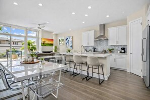 A modern kitchen with white cabinets, a central island with bar stools, a large window, and a view of the outdoors.