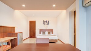 A modern hotel room with a wooden desk, a bed with a headboard, a wall-mounted macrame decoration, and a built-in air conditioning unit. - Collection O Near Mrt Cipete Raya (Jakarta)