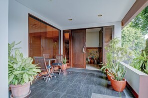 A modern outdoor seating area with a table and chairs, surrounded by potted plants and a wooden door leading to an interior space. - Collection O Near Mrt Cipete Raya (Jakarta)