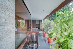 A modern outdoor seating area with a stone wall, wooden chairs, and potted plants. - Collection O Near Mrt Cipete Raya (Jakarta)