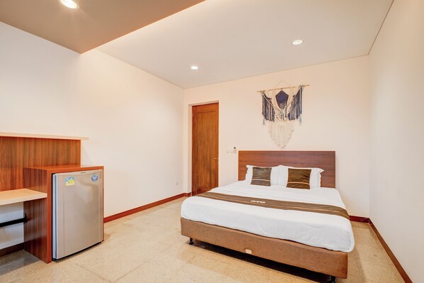 Una camera d'albergo con un letto, una scrivania in legno e un frigorifero.