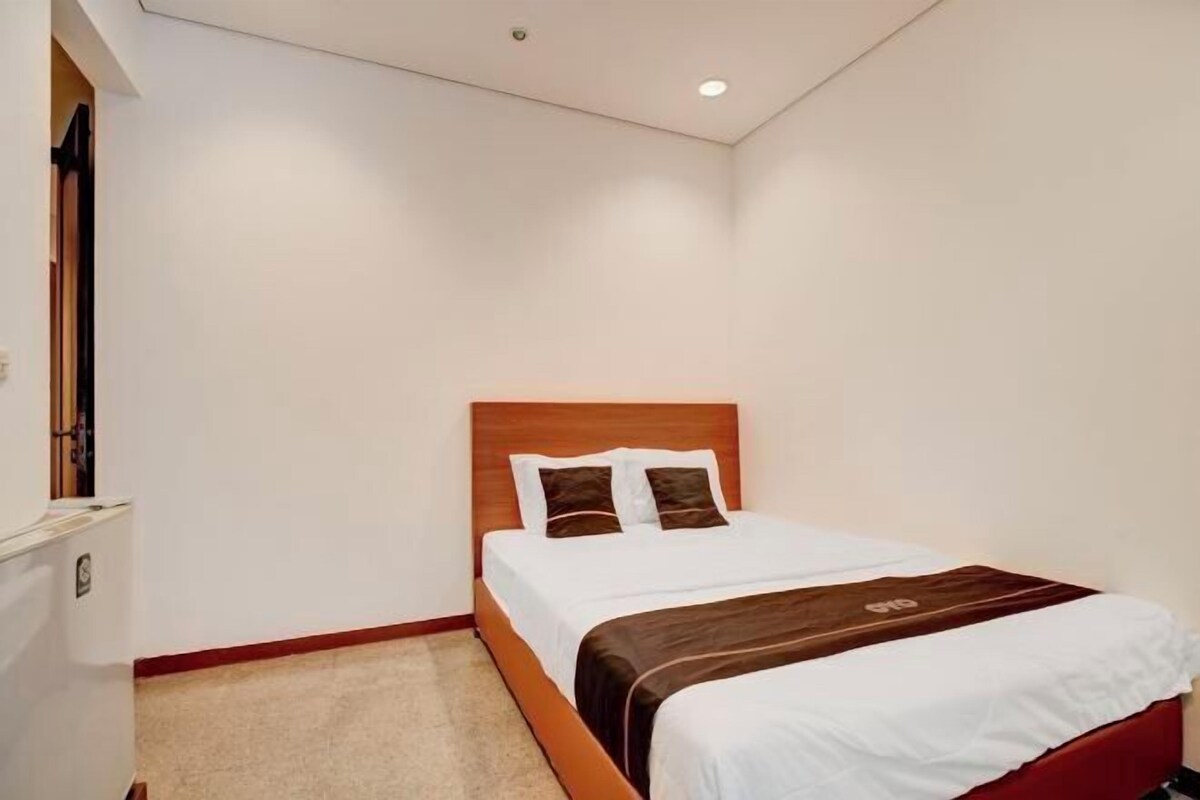 A single bed with a wooden headboard, white bedding, and a brown accent pillow.