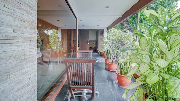 A modern outdoor seating area with a stone wall, wooden chairs, and potted plants. - Collection O Near Mrt Cipete Raya (Jakarta)