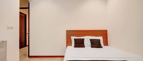 A hotel room with a wooden headboard, a bed with white and brown bedding, and a beige carpet.