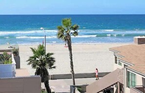 A beach view with palm trees, a person walking, and a building with a balcony.