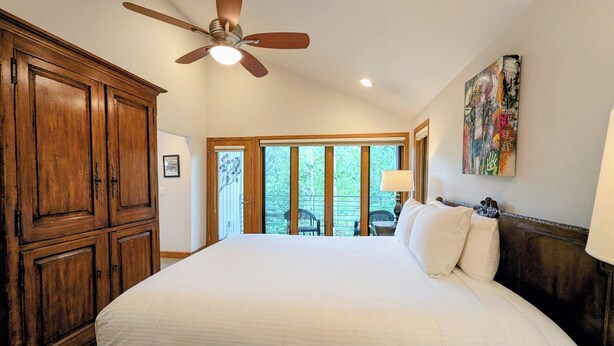 A bedroom with a large bed, wooden wardrobe, ceiling fan, and a view of the outdoors through a sliding door. - Chateaux Dumont 2702 (Keystone)