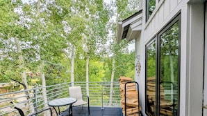 A balcony with a table and chairs, a stack of firewood, and a glass door leading to a forested area. - Chateaux Dumont 2702 (Keystone)