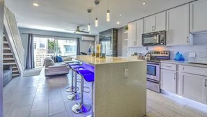 A modern kitchen with a central island, stainless steel appliances, and a bar area with blue stools.