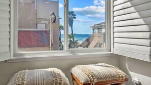 A room with a large window overlooking a beach, two cushioned stools, and a white wall.