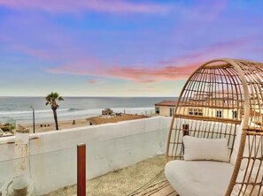 Un balcón con una silla de mimbre que da a una playa y un edificio.