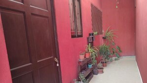 A red building with a wooden door and a tiled floor. There are potted plants along the wall and a window with a curtain. - Centrally located and furnished apartment for short stays (San José)