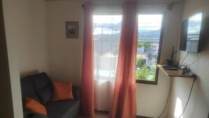 A living room with a sofa, curtains, a TV, and a view of the outdoors. - Centrally located and furnished apartment for short stays (San José)